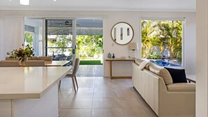 A modern living room with a large window, a sofa, a dining table, and a kitchen area. - The Art House @ Beachside (Yaroomba)