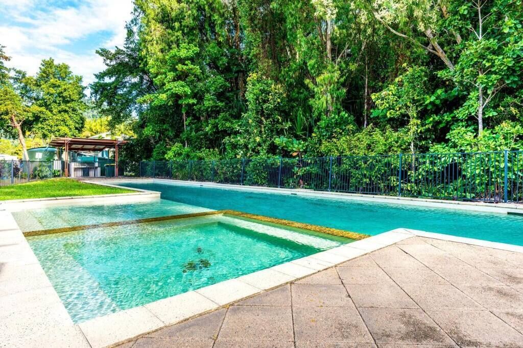 Une piscine rectangulaire à l’eau d’un bleu limpide, entourée d’une terrasse dallée et d’une clôture en métal.