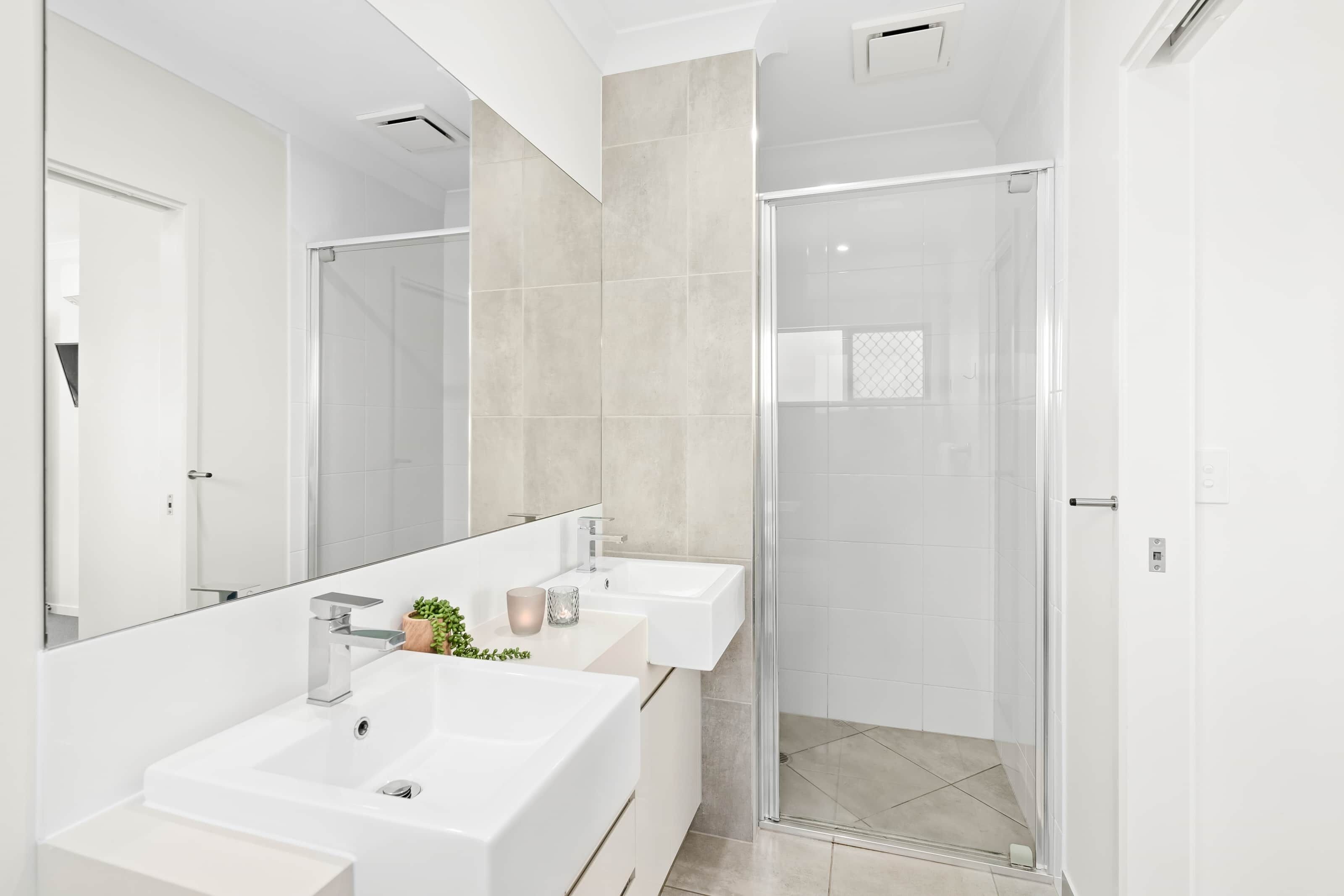 Un baño moderno con dos lavamanos, cabina de ducha de vidrio y un espejo grande.