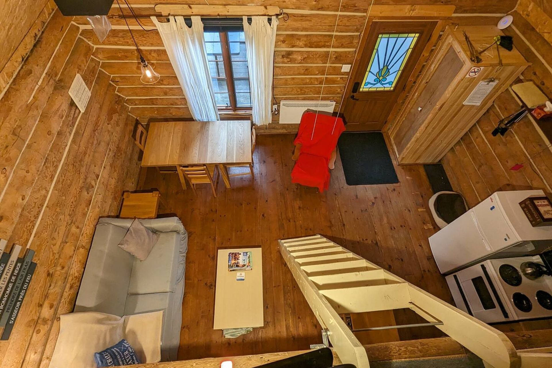 A cabin interior with a dining area, a red sofa, a staircase, and a kitchen.