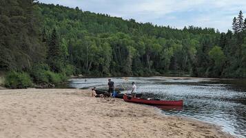 A sandy beach with a river, a red canoe, and people.