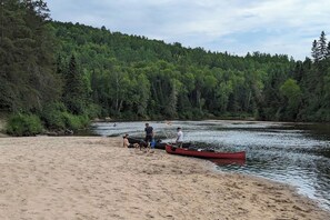 A sandy beach with a river, a red canoe, and people.