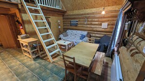 A cozy cabin interior with a wooden floor, a dining table, a sofa, a ladder, and a sign listing activities.
