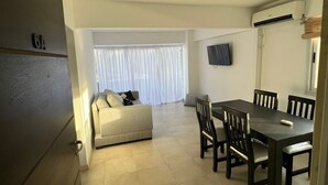 A spacious living area with a sofa, dining table, and chairs. There is a TV mounted on the wall and an air conditioning unit. - Departamento Hermosa Vista Mendoza (Mendoza)