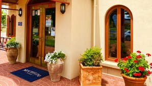 A building entrance with a wooden overhang, a door with glass panels, and a blue mat with "MIGUEL WINES" on it. - Tuscan Villa in Myrtleford (Myrtleford)