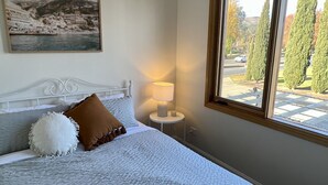 A neatly made bed with a white and gray textured blanket, a brown pillow, and a white fluffy pillow. There is a bedside table with a lamp and a framed picture on the wall above the bed. - Tuscan Villa in Myrtleford (Myrtleford)