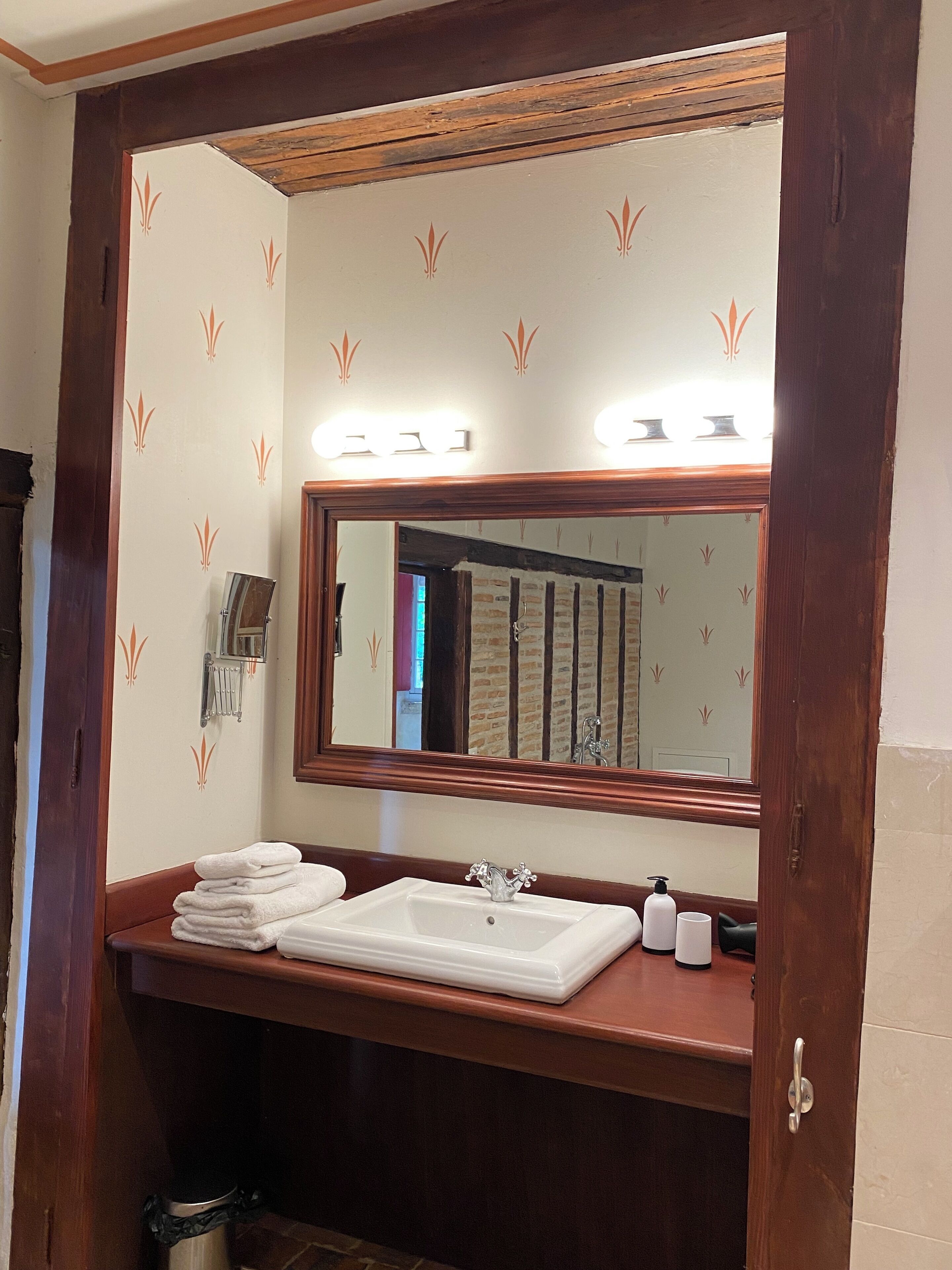 A bathroom with a wooden vanity, a large mirror, and a towel stack.