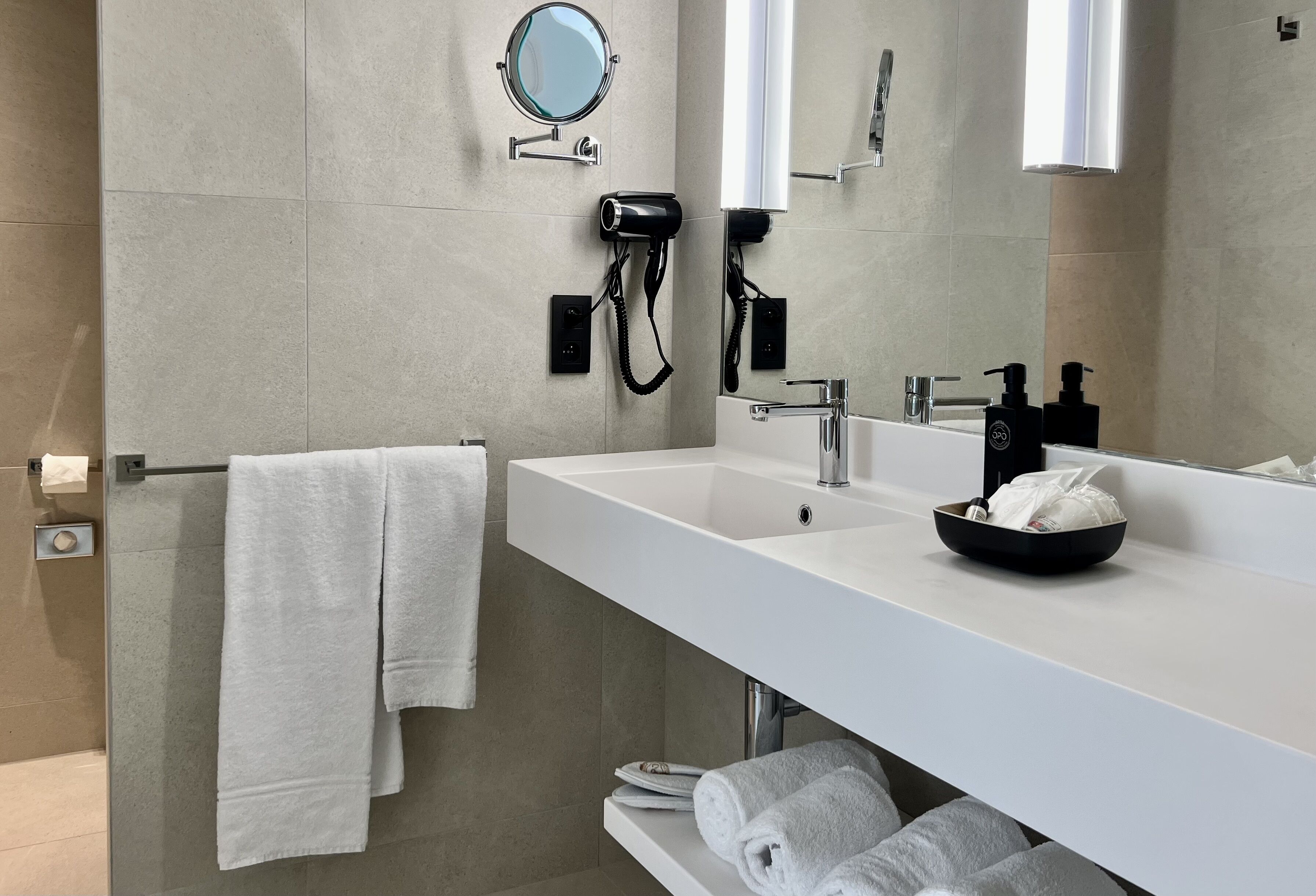 Une salle de bain moderne avec un lavabo blanc, un miroir rond, un sèche-cheveux et un porte-serviettes.