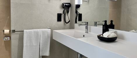 A modern bathroom with a white sink, a round mirror, a hairdryer, and a towel rack.