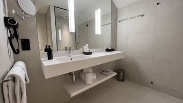Un baño moderno con tocador blanco, un espejo grande y zona de ducha.