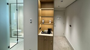 Una habitación de hotel moderna con cabina de ducha de vidrio, un mueble de madera con estantes y piso alfombrado.