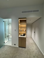 Una habitación de hotel moderna con cabina de ducha de vidrio, un mueble de madera con estantes y piso alfombrado.