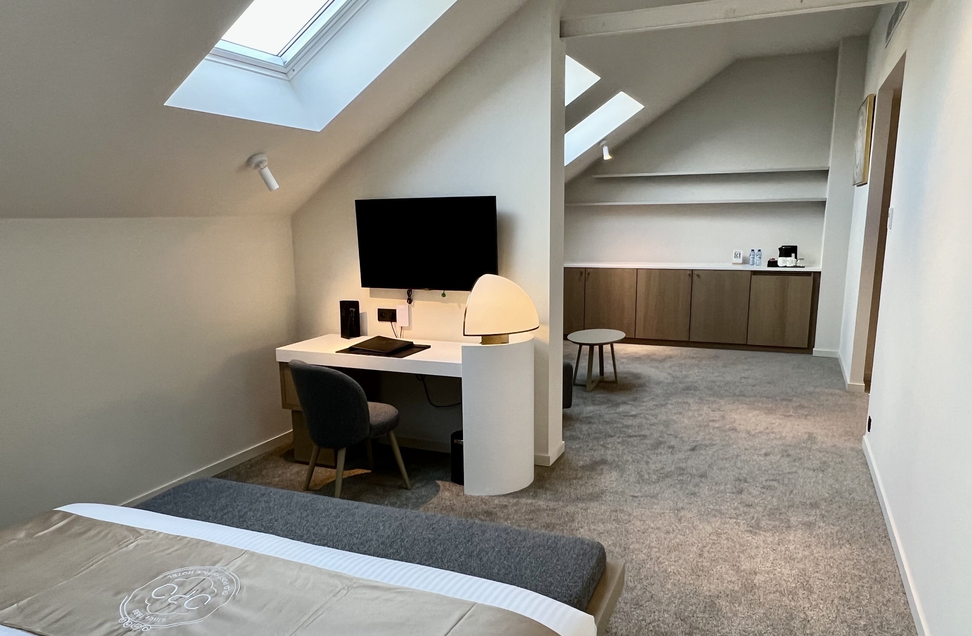 Una habitación compacta y moderna con tragaluz, un escritorio con silla, una cama y una pequeña mesa redonda.