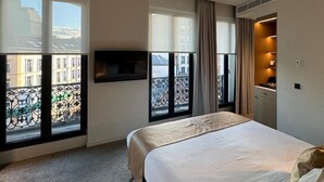Habitación de hotel con una cama grande, un televisor montado en la pared y un balcón con vistas a edificios.