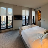 Et hotelværelse med en stor seng, et fjernsyn ophængt på væggen og en balkon med udsigt til bygninger.