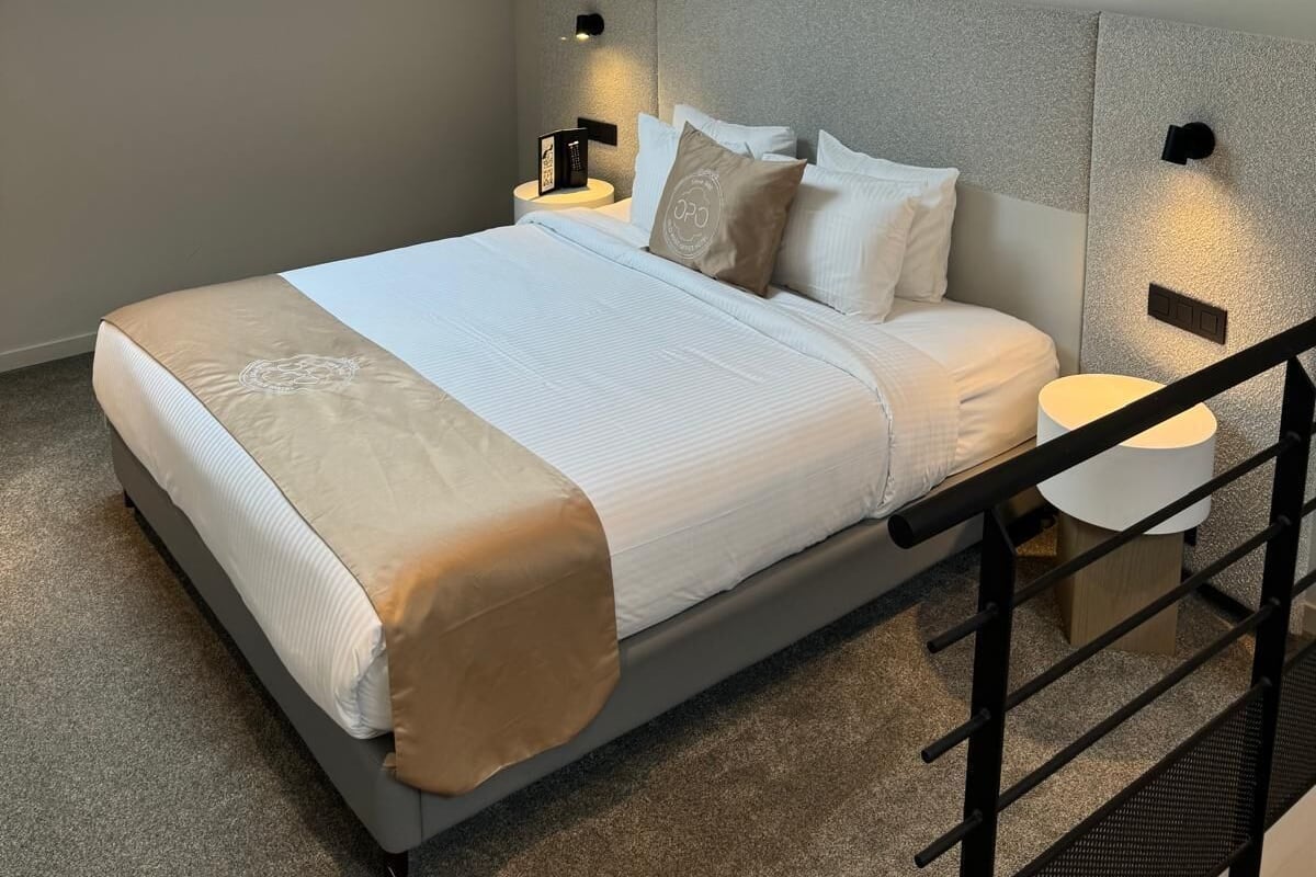 Une chambre à coucher moderne avec une lucarne, un lit recouvert de linge de lit blanc, deux tables de chevet avec des lampes et un escalier.