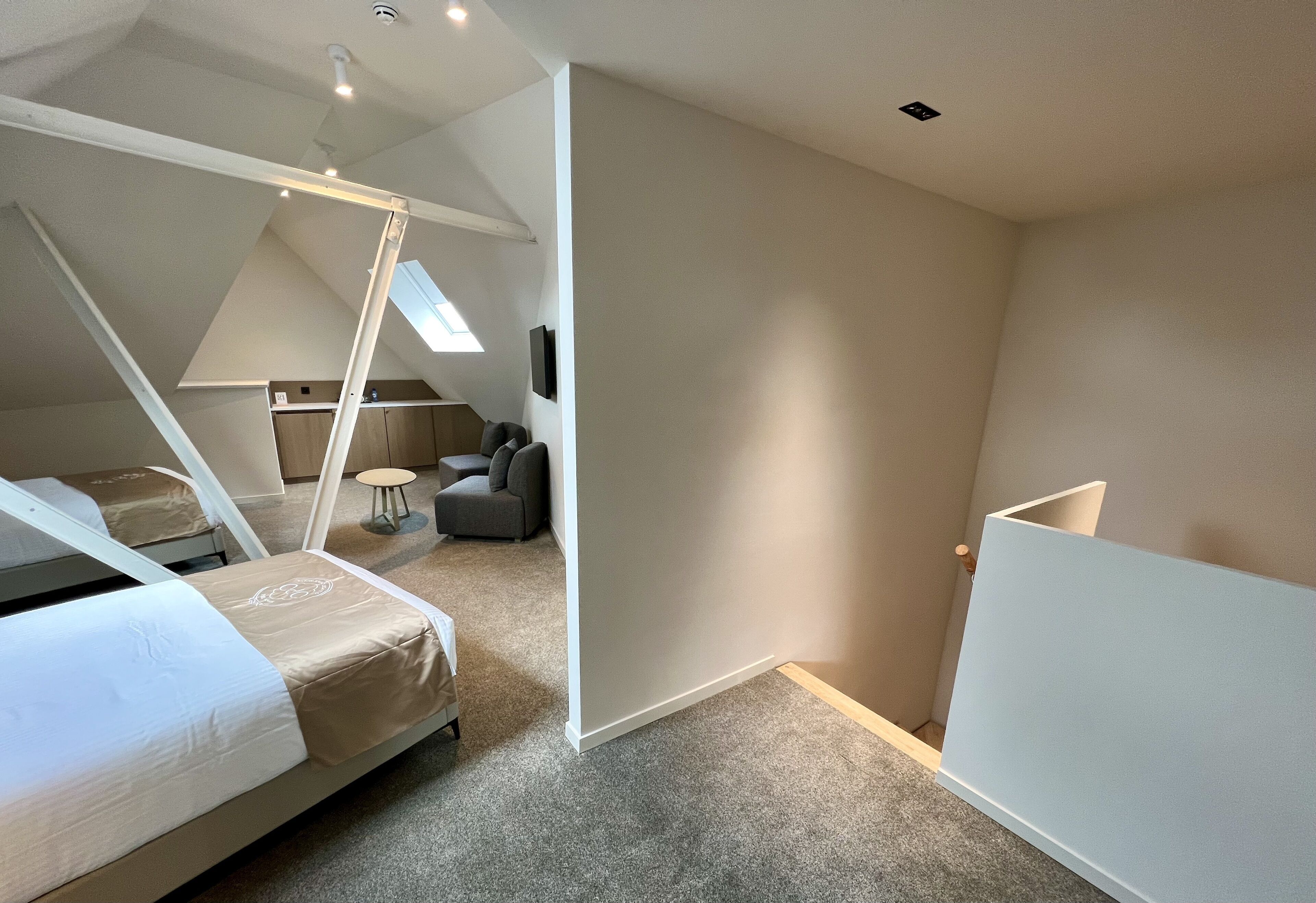 A modern, well-lit attic bedroom with a bed, a small seating area, and a skylight.