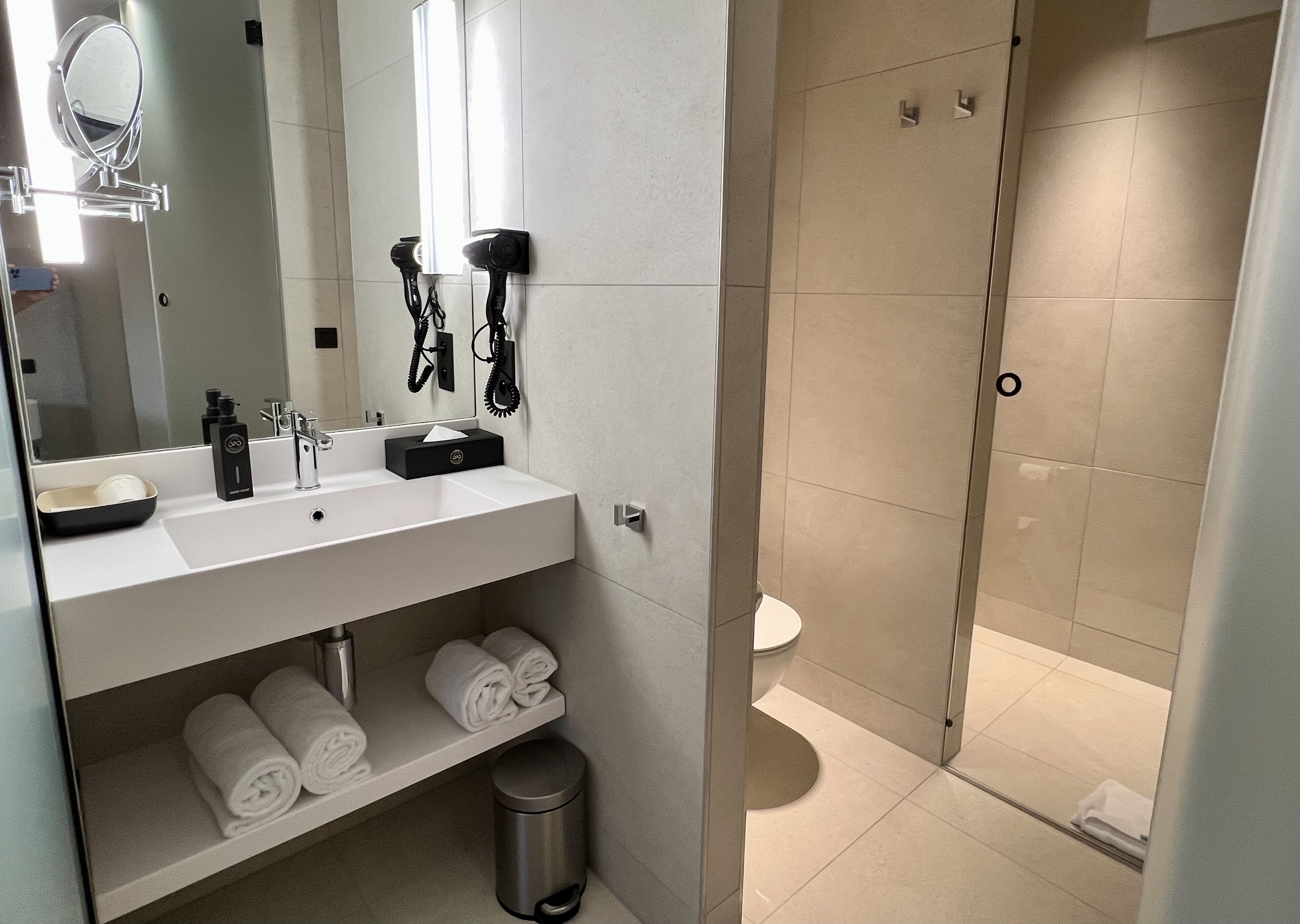 A modern bathroom with a white sink, mirror, hairdryer, and towel rack.