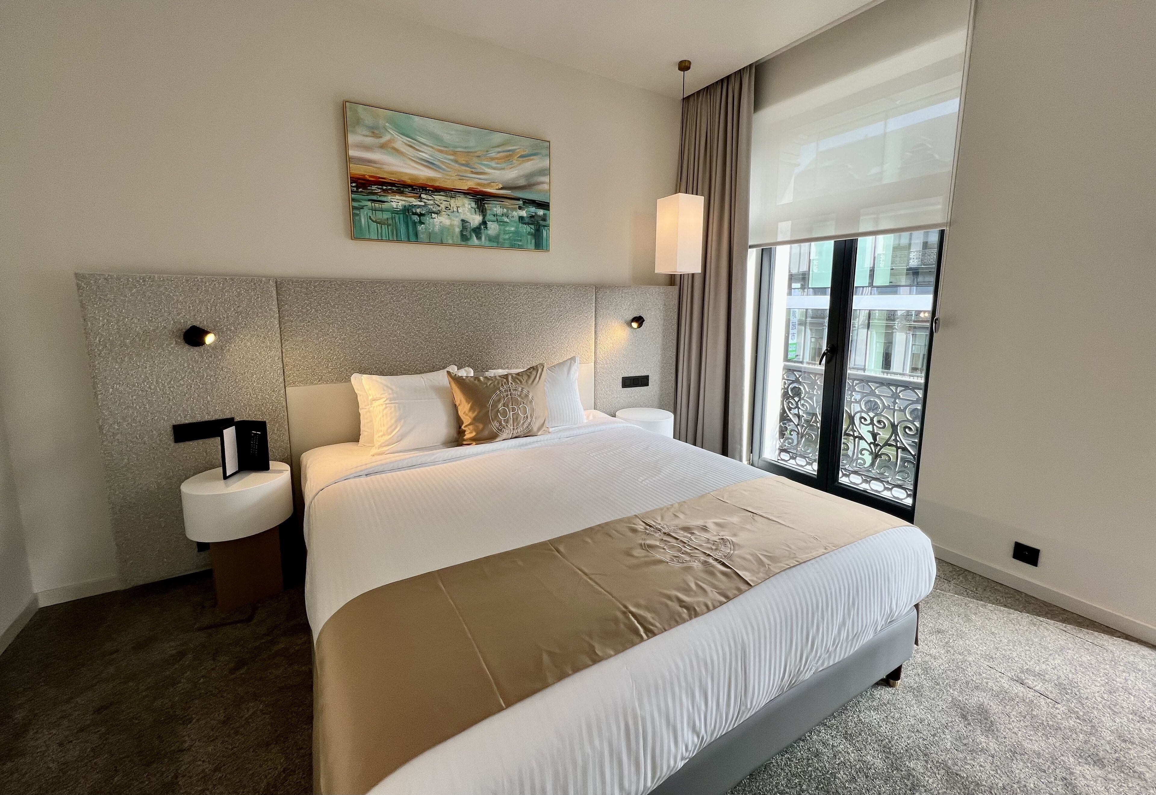 Quarto de hotel moderno com cama grande, mesa de cabeceira, quadro na parede e janela com vista.
