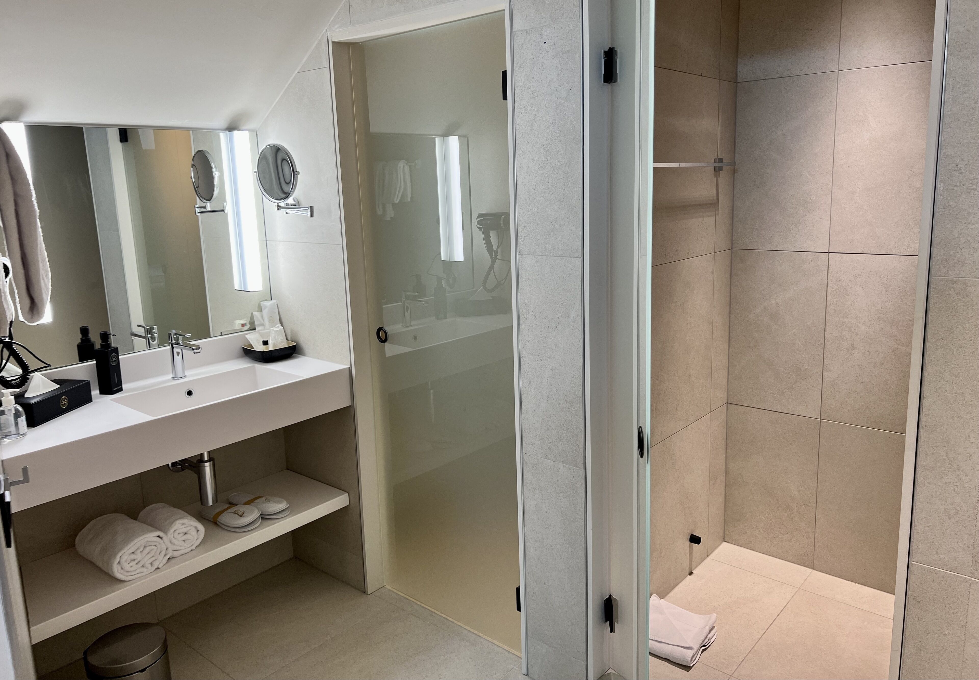 Une salle de bain moderne avec une douche à parois de verre, un lavabo avec un miroir et des serviettes soigneusement pliées sur une étagère.