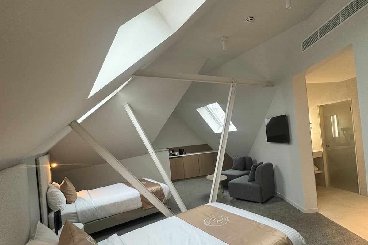 Une chambre de style loft moderne, avec un plafond en pente, deux lits, un coin salon et un téléviseur.