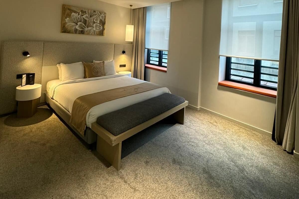 Une chambre d’hôtel moderne avec un grand lit, des lampes de chevet, un tableau au mur et une fenêtre avec des rideaux.