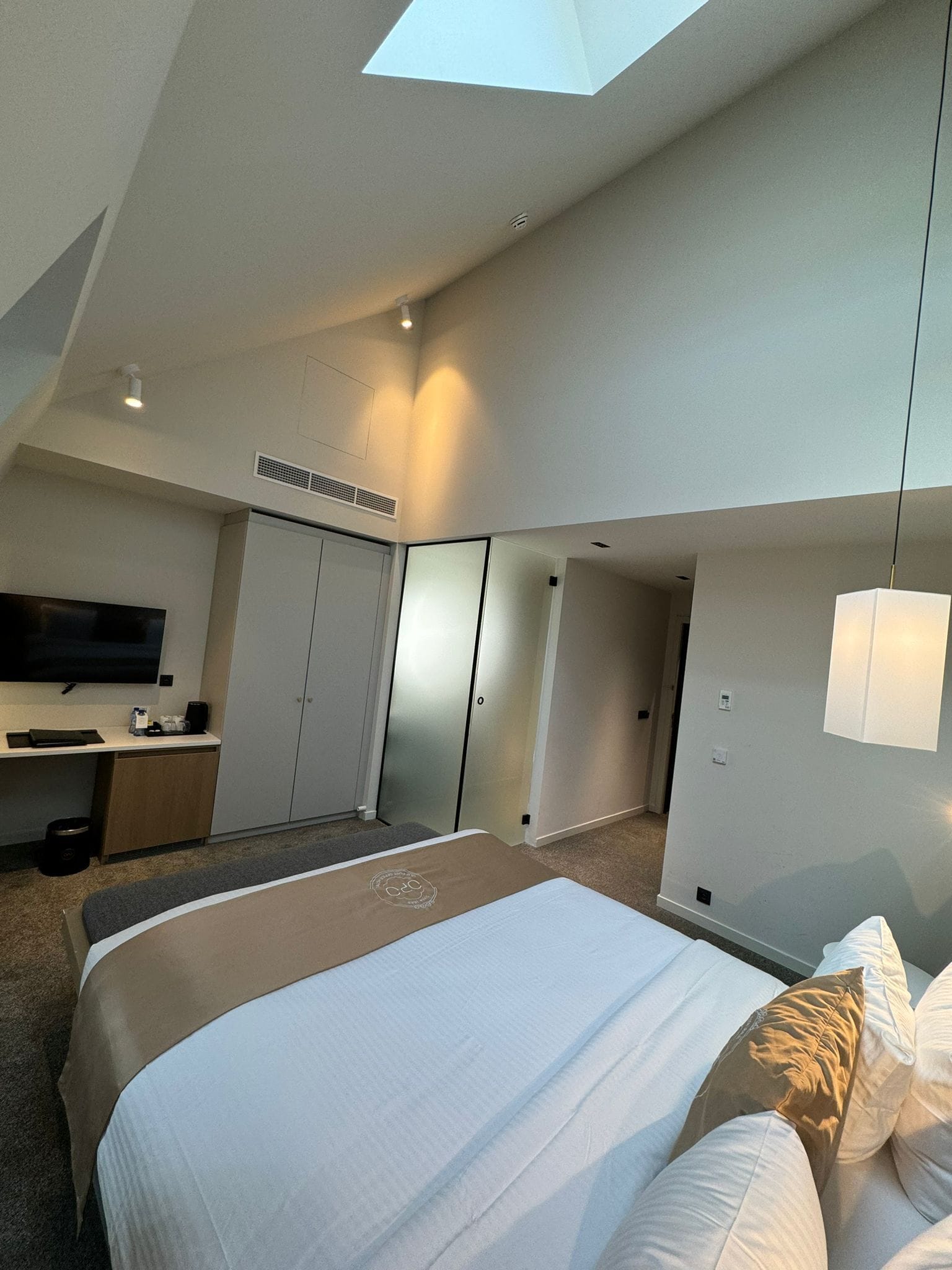 A modern hotel room with a large bed, a flat-screen TV, a desk with a chair, and a wardrobe.