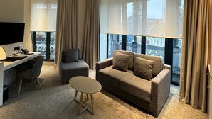 Una habitación de hotel con sofá, sillón, escritorio y una pequeña mesa redonda.