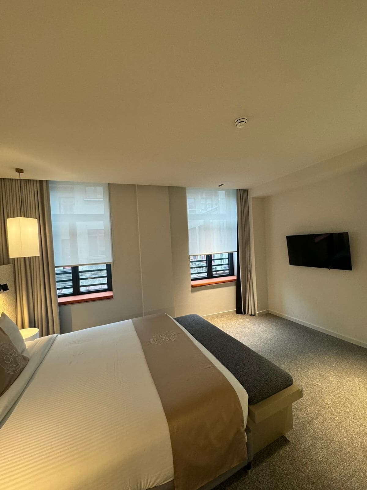 A hotel room with a large bed, a smaller bed, a TV mounted on the wall, and a window with a view of the outside.