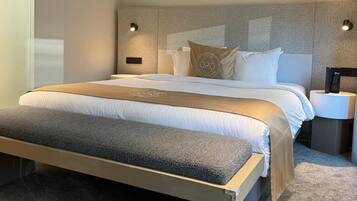 Ein modernes Schlafzimmer mit einem großen Bett, einem an der Wand befestigten Kopfteil mit integrierter Beleuchtung, einem Nachttisch mit Fernbedienung und einem floralen Kunstwerk.