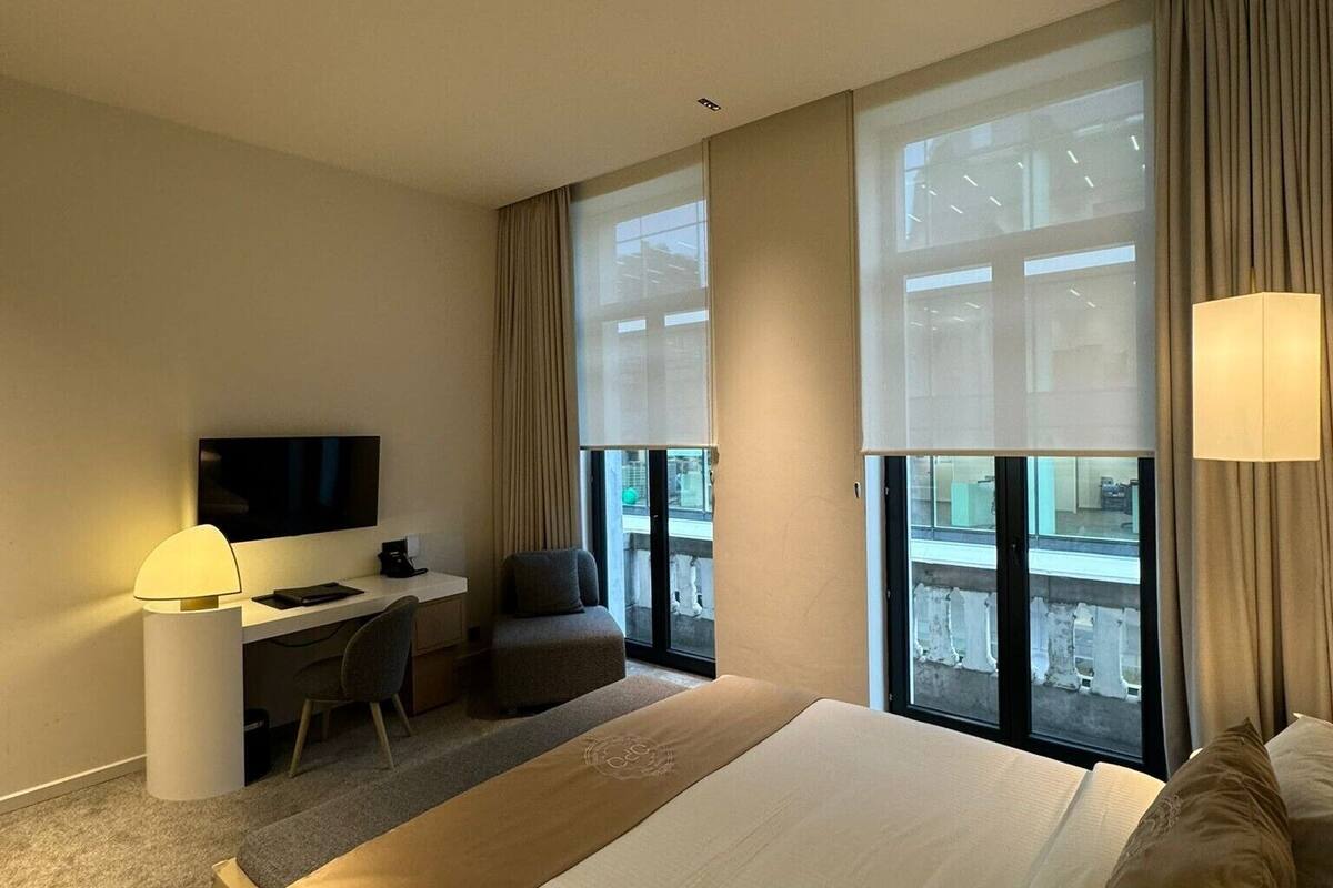 Une chambre d’hôtel avec un grand lit, un bureau avec une chaise, une télévision et de grandes fenêtres avec des rideaux.