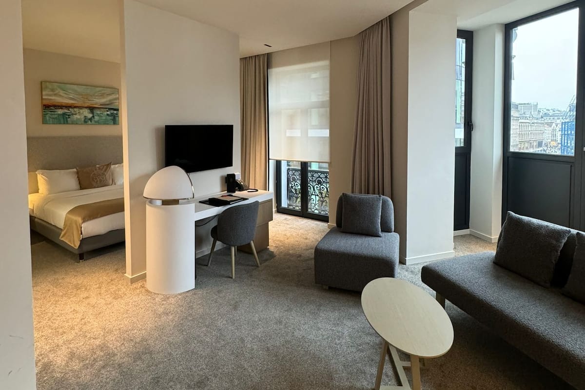 Une chambre d’hôtel moderne équipée d’un lit, d’un bureau, d’une télévision, d’un canapé et d’un balcon offrant une vue sur la ville.