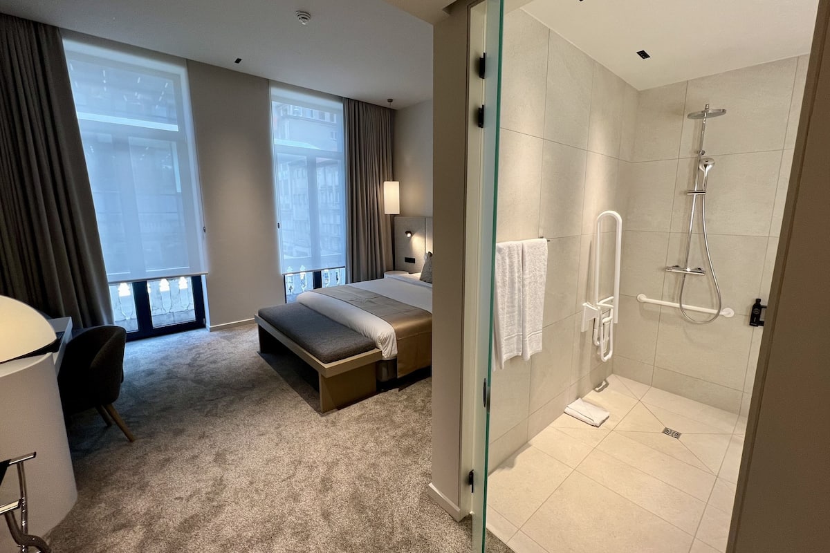 Une chambre d’hôtel avec un grand lit, un bureau, une chaise, une douche en verre et une vue sur la ville.