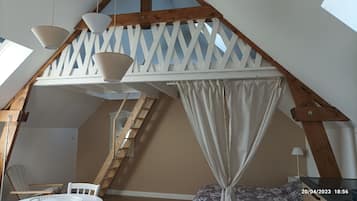 Cozy attic bedroom with a sloped ceiling and a wooden staircase, featuring a comfortable bed with a canopy, a chair, and a small table.