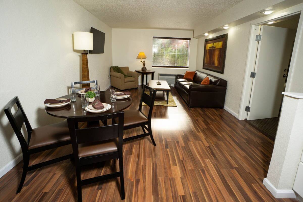 A dining area with a round table, chairs, and a sofa in the background.