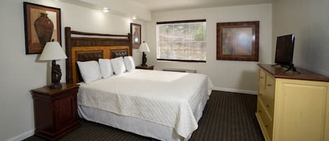 A hotel room with a large bed, a wooden headboard, a television on a stand, a dresser, and two framed pictures on the wall.