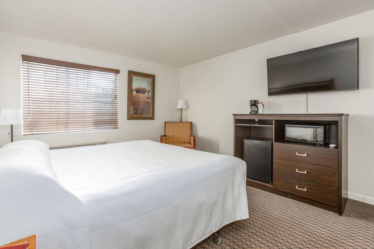 A hotel room with a bed, a flat-screen TV, a microwave, a coffee maker, and a chair.