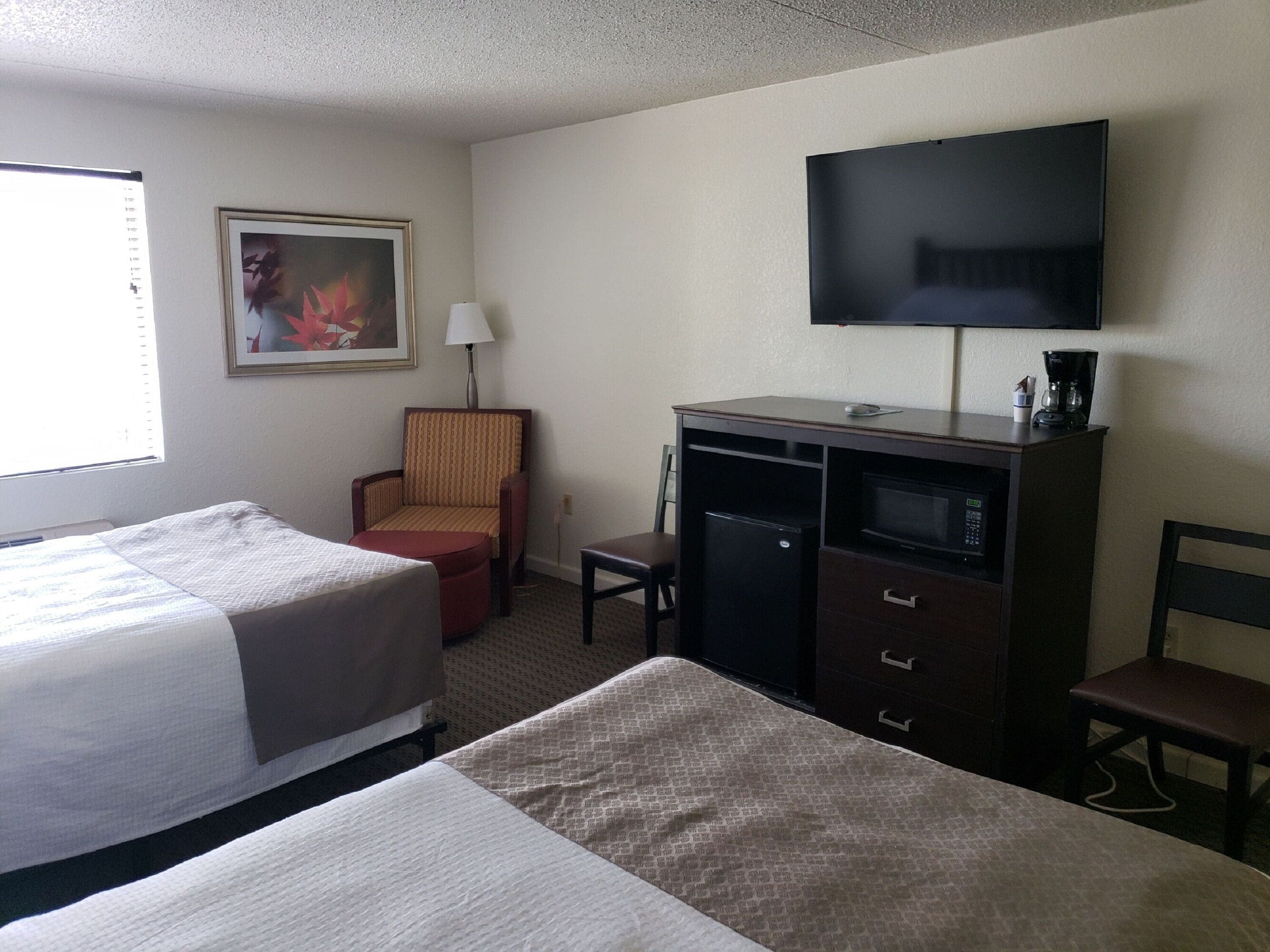 A hotel room with two beds, a desk, a chair, a television, and a painting on the wall.