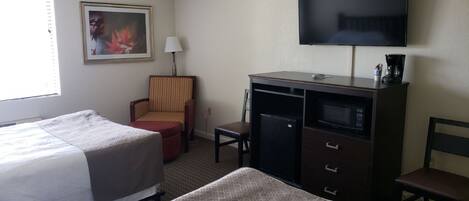 A hotel room with two beds, a desk, a chair, a television, and a painting on the wall.