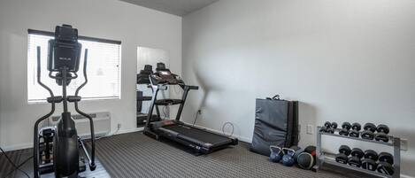A home gym with a treadmill, elliptical, and dumbbells.