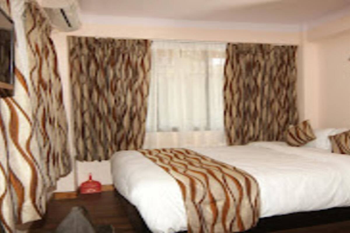 A hotel room with a large bed, curtains, a television, and a small table.