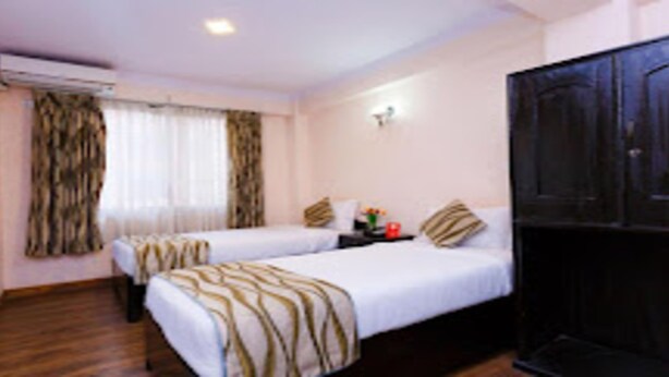 A hotel room with two beds, a large wardrobe, and a small table with a vase. - MeroStay 206 Hotel KU (Kathmandu)