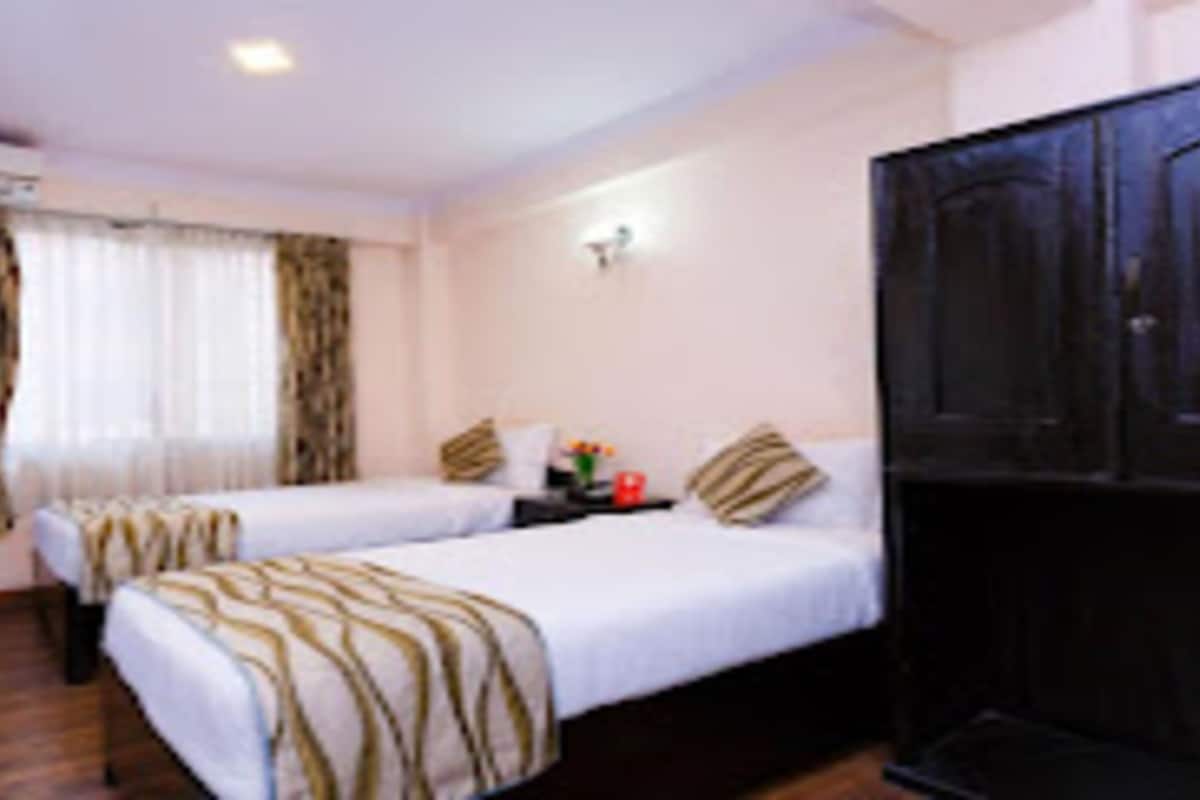 A hotel room with two beds, a large wardrobe, and a small table with a vase.