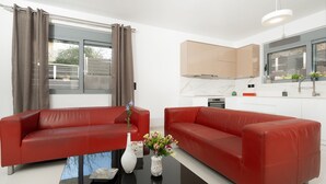 A modern living room with two red leather sofas, a glass coffee table, and a vase with flowers. - MTC-AN Apartment by the sea and Airport (Markopoulo Mesogaias)