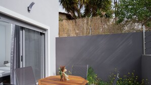 A modern outdoor patio with a wooden table and chairs, a sliding glass door, and a bamboo fence. - MTC-AN Apartment by the sea and Airport (Markopoulo Mesogaias)