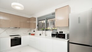A modern kitchen with white cabinets, a built-in oven, a coffee maker, and a microwave. - MTC-AN Apartment by the sea and Airport (Markopoulo Mesogaias)
