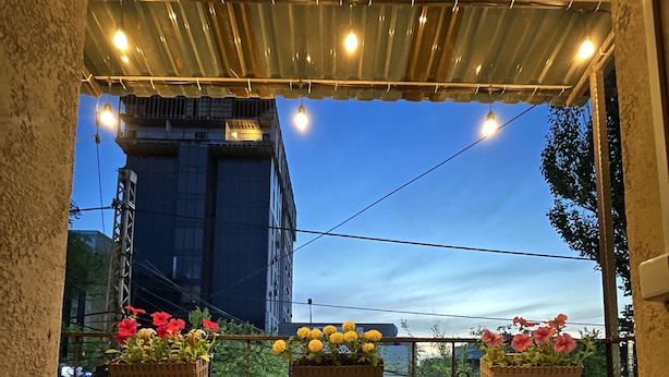 An outdoor patio with a wooden table and two chairs, surrounded by potted plants with red and yellow flowers. - People Hostel (Bishkek)