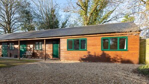 A wooden building with a gravel driveway, a green door, and two windows with green frames. - Secluded stables with parking in grounds of home in the heart of the new forest  (Burley, Nr Ringwood)
