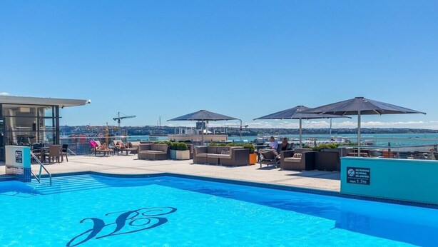 A rooftop pool with lounge chairs and umbrellas, overlooking a body of water.