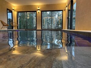 Una piscina interior con vistas despejadas a árboles a través de amplias puertas de cristal.